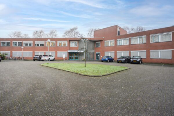 Vooraanzicht van het rode bakstenen gebouw aan de Christiaan Krammlaan met parkeervakken en fietsenrekken.